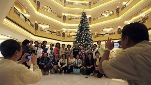 Tourists pose to have their photos taken in front of a Christmas tree which has been decked out with $11 million worth of gold.