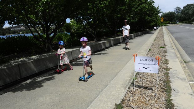 Zoe Burrowes, sister Ella and their dad Ian, of Melbourne, scoot past a snake warning sign.