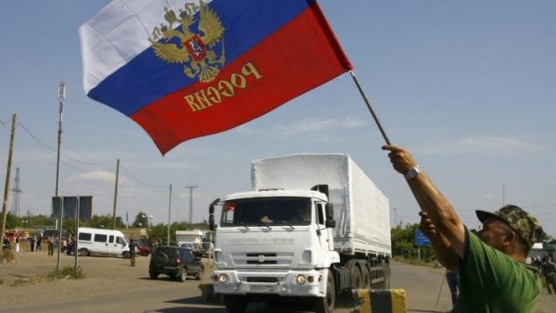 A resident holds a Russian flag as a truck from the previous aid convoy crosses the Ukrainian border. Moscow has vowed to send another.
