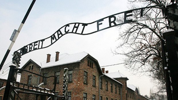 Tourists pause near the gates of the former Nazi death camp at Auschwitz in Poland, where a replica of the stolen sign has been temporarily erected.