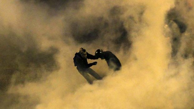 Running riot ... protesters are seen through smoke from a tear gas canister thrown by police in Athens.
