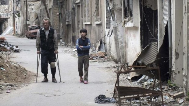 Ceasefire on the table: Residents walk by damaged buildings in the besieged area of Homs.