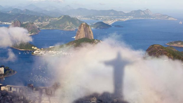 The shadow of the Christ the Redeemer statue floats over Rio de Janeiro and Sugar Loaf.
