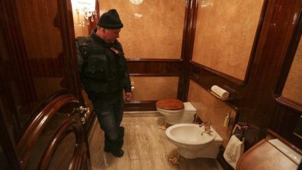 A man stands inside a lavatory as anti-government protesters and journalists walk on the grounds of the Mezhyhirya residence of Ukraine's President Viktor Yanukovich.