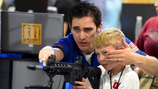 Brett Throckmorten of Barnes Bullets shows Logan Wingo how to sight down an electronic rifle in the trade booth area during the National Rifle Association's annual meeting in Nashville, Tennessee.