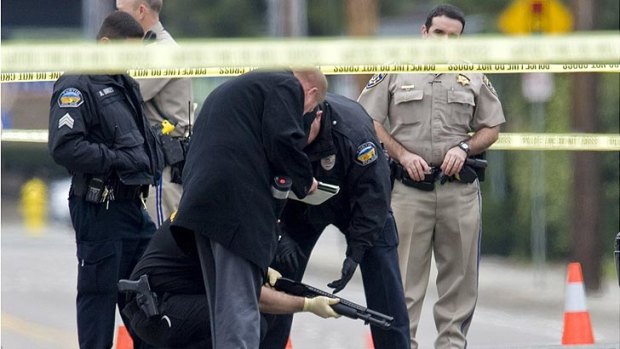 Police investigators examine a gun laying in the street in Orange, California, near where a body laid moments before.