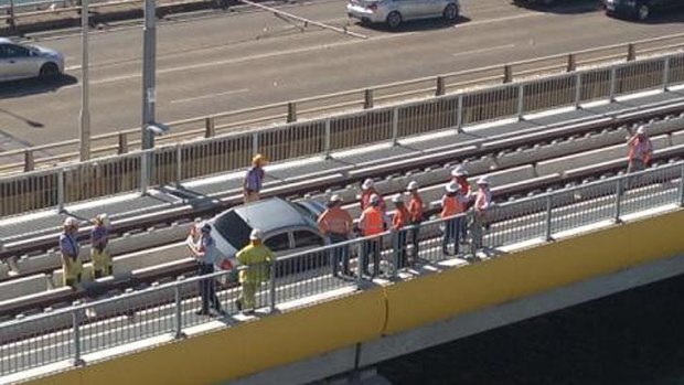 Workers try to remove a car from light rail tracks on the Sundale Bridge at Southport.