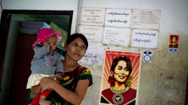 A woman in Burma holds her baby as she waits to register to vote. On the wall is a poster of opposition leader Aung Sun Suu Kyi, who is boycotting the election.