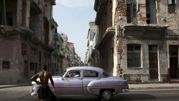 A car passes a pedestrian in the street in Havana, Cuba.