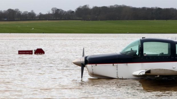 A plane sits in flood water by submerged warning signs following heavy rain, at Redhill Aerodrome in Surrey, England,.