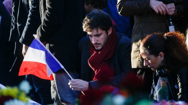A mourner holds a French national flag as he pays his respects to victims of the terrorist attacks, at Place de la Republique in Paris.