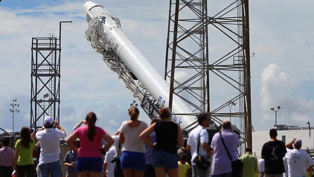 People watch as a SpaceX Falcon 9 rocket attached to the cargo-only capsule called Dragon is raised into launch position.