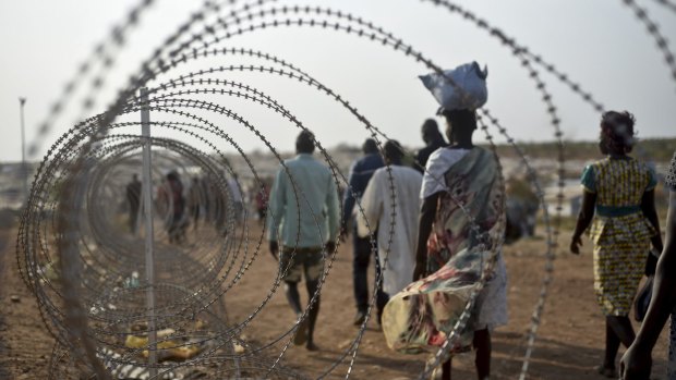Displaced people walk next to a razor wire fence at the UN base in Juba, South Sudan. 