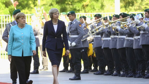 Angela Merkel and Theresa May review an honour guard after the latter's arrival in Berlin. Mrs May's next stop will be Paris.