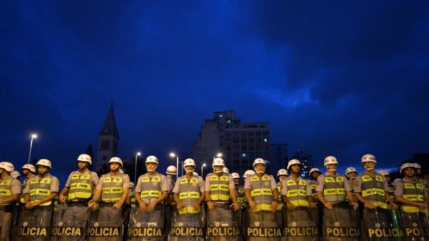 Police officers stand guard in Sao Paulo as demonstrators march against the upcoming World Cup 