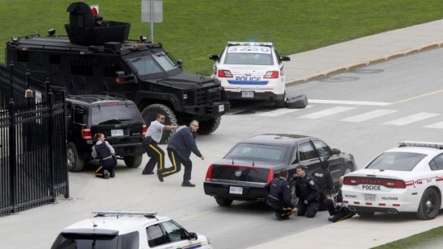 Police officers take cover near Parliament Hill following the shooting.