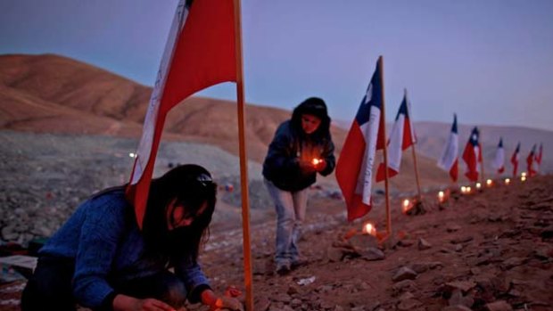 Women light candles next to Chilean flags representing the 33 trapped miners.