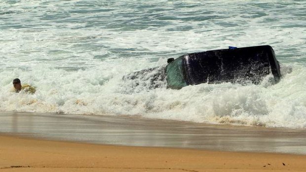 A man attempts to pull the abandoned four-wheel-drive from Stockton Beach.
