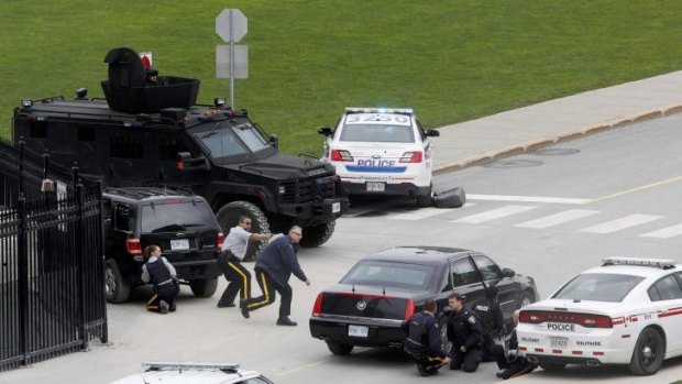 Police officers take cover near Parliament Hilll following the shooting.