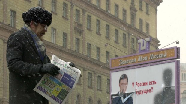 A man hands out free advertising newspapers in Moscow while behind him looms the Federal Security Service building. The Federal Security Service is the former KGB.