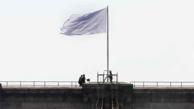 New York City Police officers stand at the base of a white flag flying atop the west tower of New York's Brooklyn Bridge.