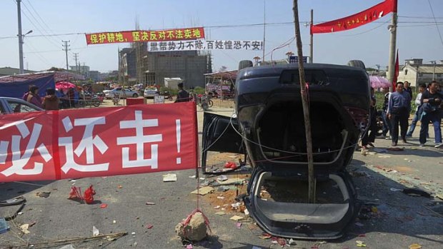 A red sign proclaiming 'We must retaliate' is displayed next to an overturned car at the entrance of Shangpu village in China's Guangdong province.