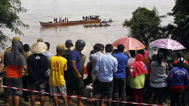 Villagers gather on the banks of Mekong river as rescue personnel on boats search the plane crash site.