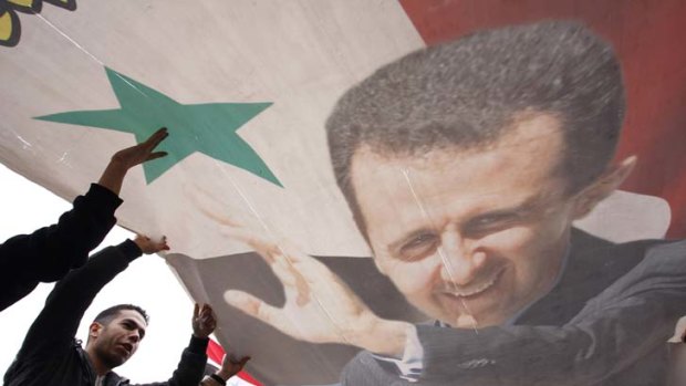 Display of loyalty ... regime supporters wave a portrait of President Bashar al-Assad at a rally in Damascus.