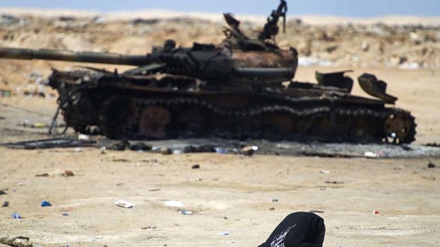 A Libyan rebel at prayer in front of a burnt-out tank.
