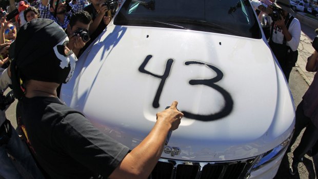 A protester spray-paints "43" on the hood of a car belonging to Congressman Jorge Salgado on Wednesday during a protest in Chilpancingo, Guerrero, to support the missing 43 trainee teachers.