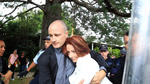 Close call ... Julia Gillard protected by one of her security detail as she is rushed to her car.