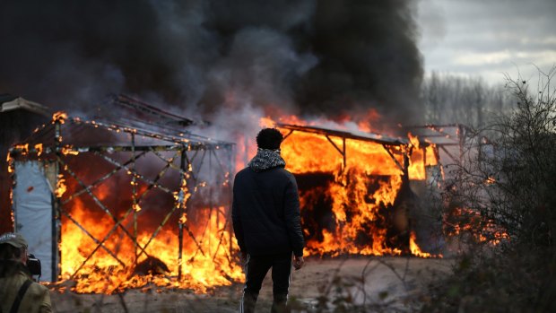 A migrant watches as a hut burns as police officers clear part of the 'Jungle' migrant camp. 