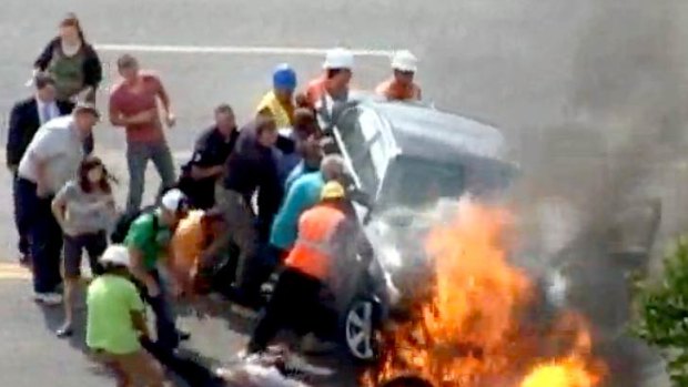 Bystanders brave the threat of an explosion as they lift the flaming BMW to rescue an injured motorcyclist.