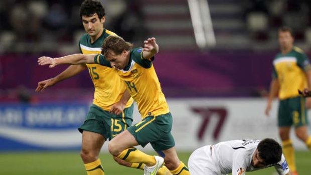 Australia's Mile Jedinak (L) watches as teammate Brett Holman fights for the ball with Uzbekistan's Azizbek Haydarov.
