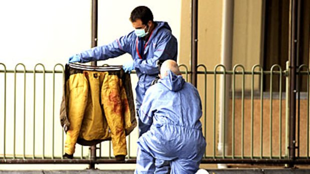 Forensics officers inspect a blood-soaked jacket at the scene.