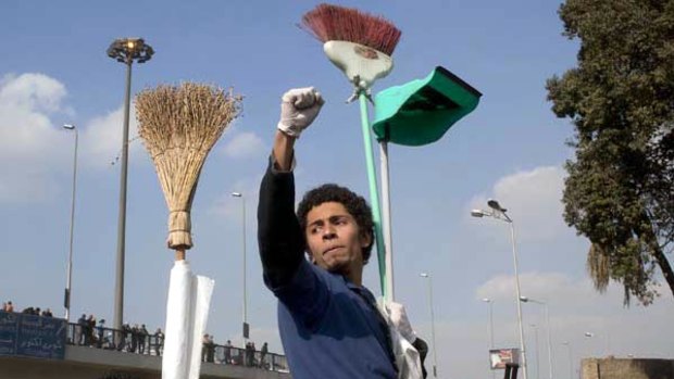 Egyptian volunteers holds their brooms high on their way to remove debris and garbage from Cairo's Tahrir Square