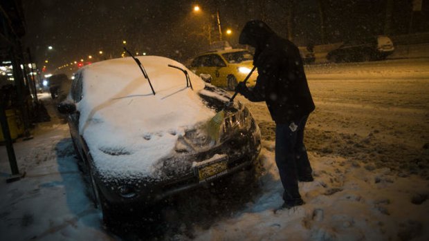 A motorist clears snow from his car in New York.