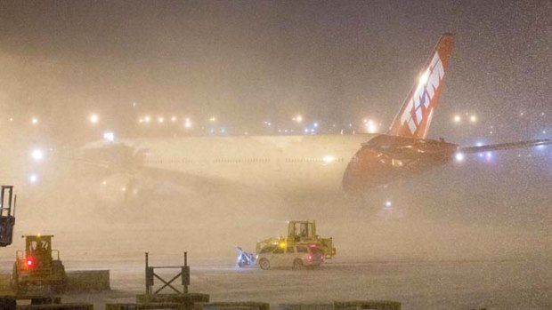 A plane sits shrouded by snow as ploughs work around it at John F. Kennedy International Airport.