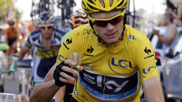 Overall leader's yellow jersey Britain's Christopher Froome holds a glass of Champagne as he rides next to his team car.