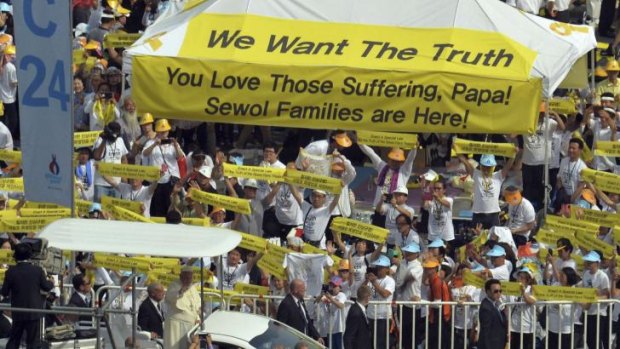 Victims' families hold up banners to Pope Francis as he passes in  the Popemobile.