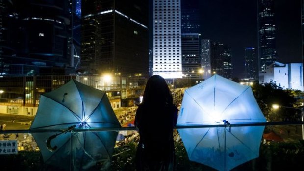 A woman stands between two umbrellas as she looks over the bridge to Admiralty district in Hong Kong.