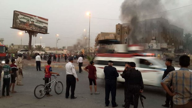 Iraqi policemen and people gather at the site of a car bomb in Talibiya in Baghdad.