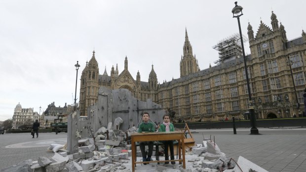 Two children whose school was bombed in Aleppo pose for pictures in a mock destroyed classroom outside the Houses of Parliament in London.