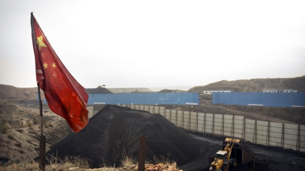 In this Nov. 4, 2015 photo, a Chinese flag stands in the breeze as a loader moves coal at a coal mine near Ordos in northern China's Inner Mongolia Autonomous Region. The annual gathering of the National People?s Congress is largely ceremonial, doing little lawmaking and instead providing a platform to publicize the Communist Party?s priorities. This year, delegates will focus on the ruling party?s new development plan - the latest chapter in a marathon effort to transform China into a middle-income economy with self-sustaining growth driven by consumer spending instead of investment, trade and heavy industry. The slowdown and Beijing's efforts to shift emphasis away from heavy industry already have slashed workforces at mines, shipyards and other employers. (AP Photo/Mark Schiefelbein)