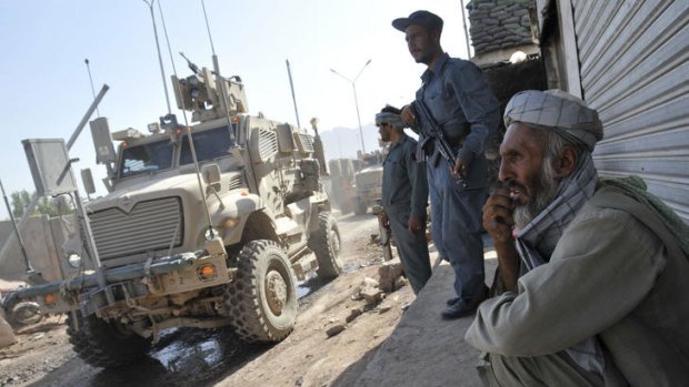 Afghan elder and armed Afghan police watch a convoy of US armored vehicle leaving the military forward base in Afghanistan.