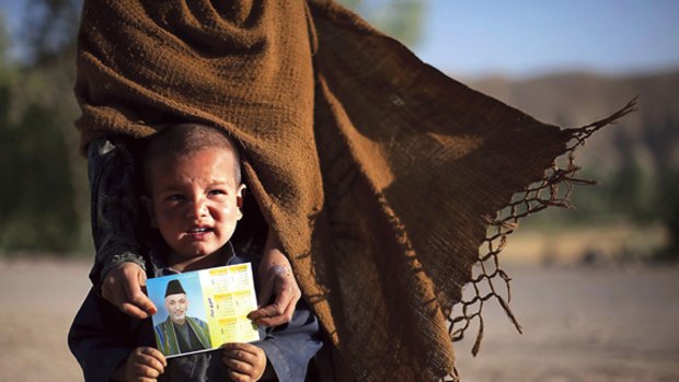 Catch them young ... an Afghan Hazara child, in the care of his sister, holds a postcard urging support for President Hamid Karzai in the elections on Thursday.