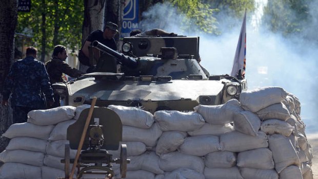 Pro-Russian armed men stand guard next to a tank at a checkpoint in the eastern Ukrainain city of Slavyans.