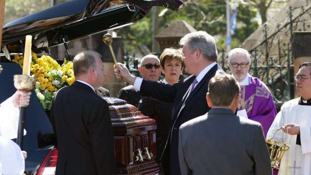 Farewell: Anthony Cummings sprinkles holy water on the casket of his father, legendary racehorse trainer Bart.