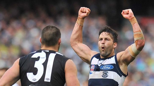 Jimmy Bartel raises his arms in triumph after scoring; Chris Dawes finds it too painful to look.