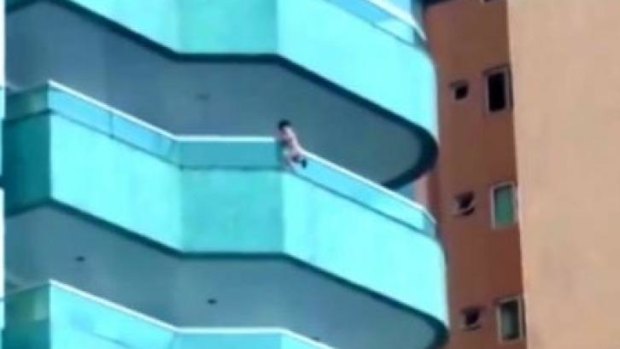 A toddler hangs from the balcony of a building in Brazil.